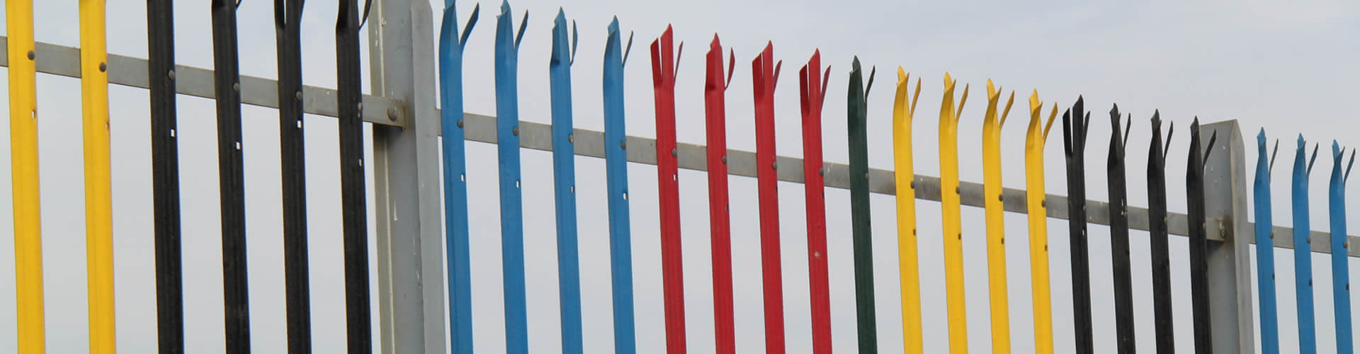 Palisade fence with RSJ beam post and D section pales. Triple pointed palisade pales are painted with black, blue, red and yellow.